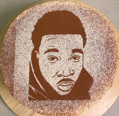 A tiramisu cake with a portrait of a person dusted on top, made with cocoa powder.